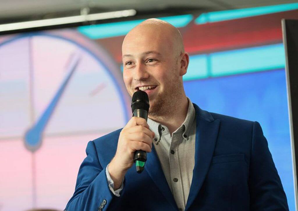 A Maximillion Human Bingo leader running an event from a stage